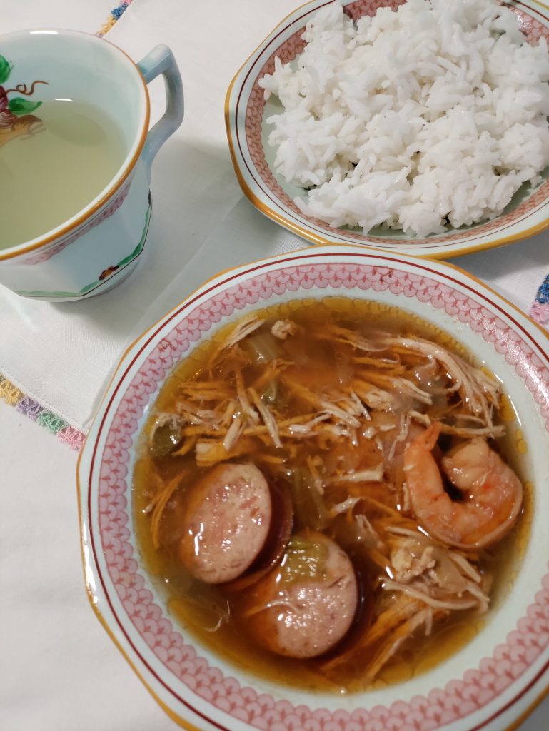 Bowl of louisiana gumbo sitting on a white cloth next to a bowl of rice and a cup of lemonade. #louisiana #gumbo #dinner #recipe #onepot