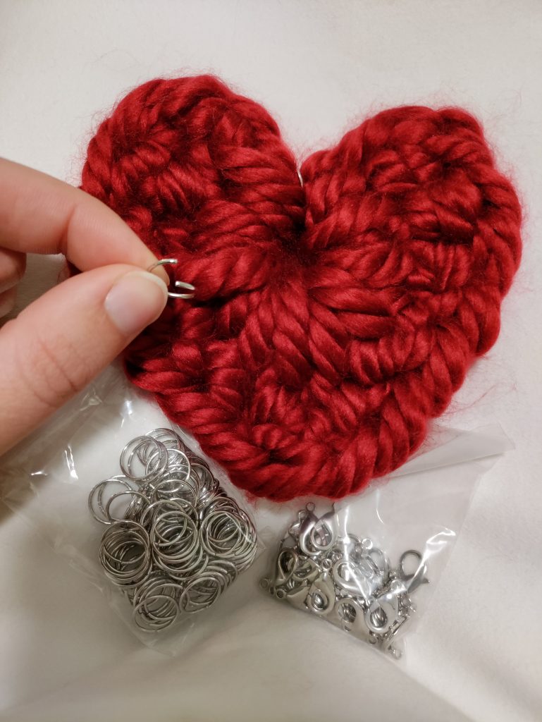 red crochet heart keychain with a hand holding an open jump ring