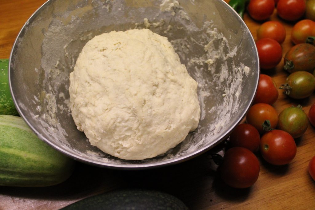 sourdough flatbread dough in a bowl next to garden fresh vegetables